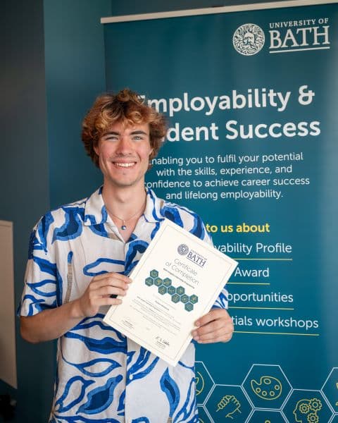Preston holding his Bath Insights internship certificate in front of a University of Bath Student Success banner
